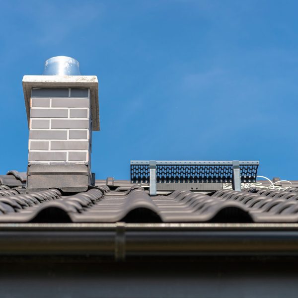 The roof of a single-family house covered with a new ceramic tile in anthracite against the blue sky. Vsible system chimney covered with tiles.