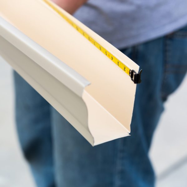 Worker Measuring An Aluminum Rain Gutter Feeding Through Seamless Shaping Machine.